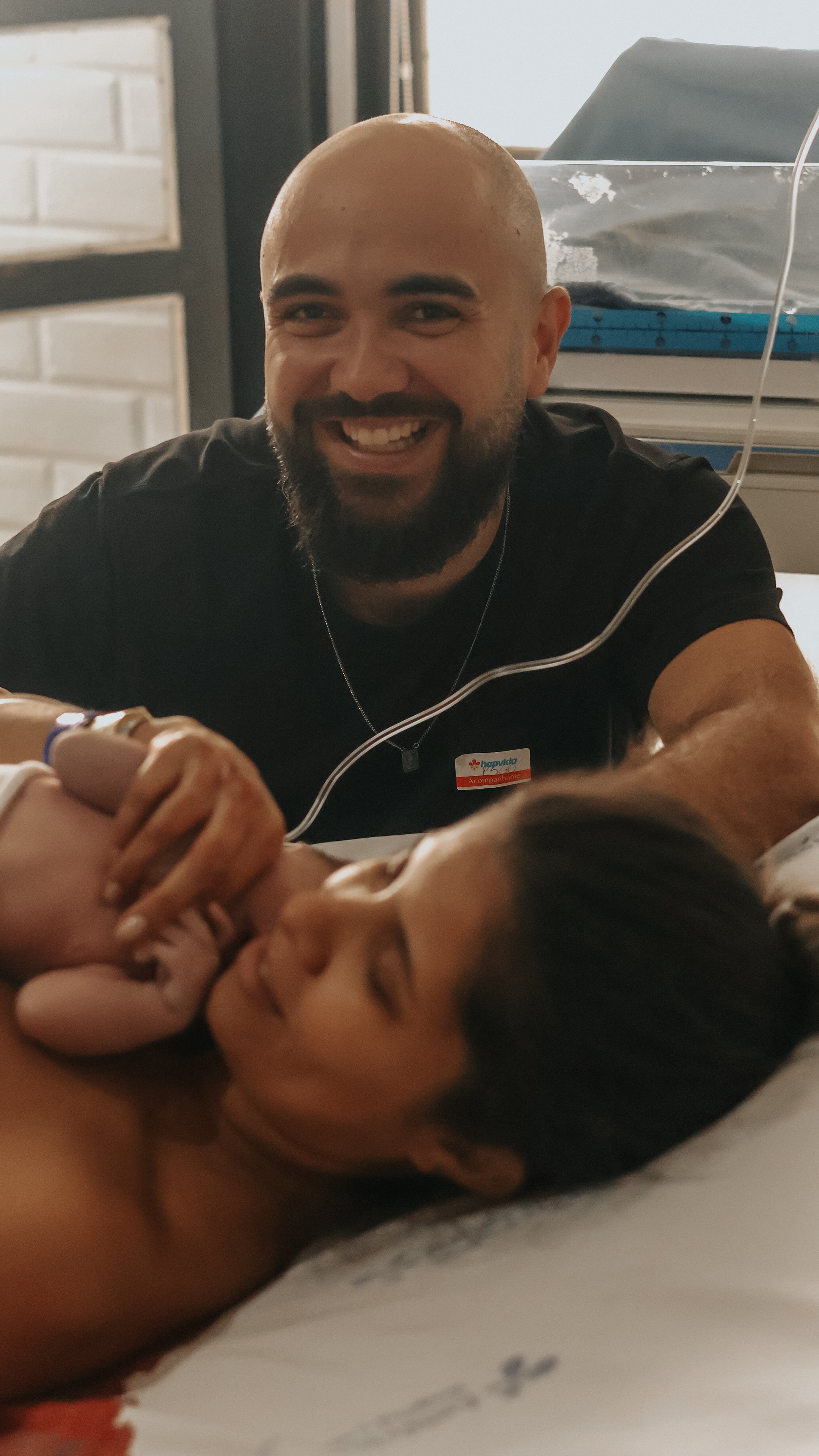 Os pais olhando para a câmera com o bebê, na suíte da maternidade